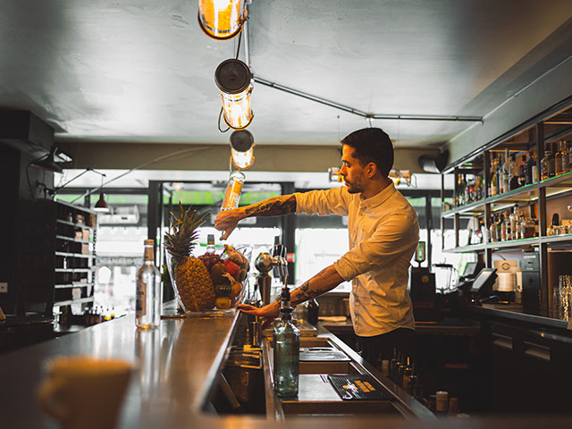 Le barman prépare un cocktail derrière le comptoir en bois de La Place Verte.