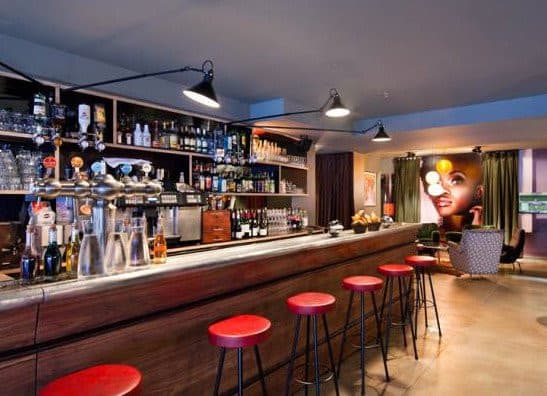 Le long bar en bois, ses tabourets rouges et sa fresque murale.